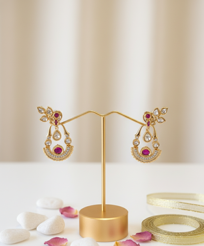 Gold earrings with pink gemstones on a gold stand against a beige background